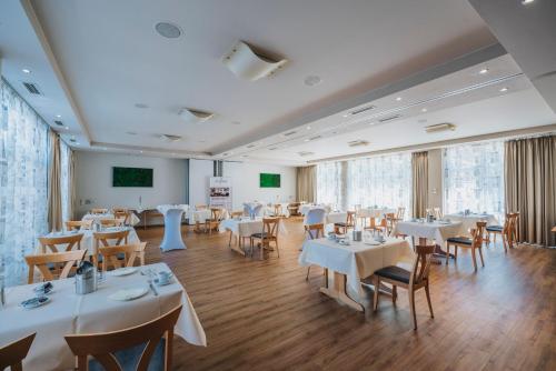 梅尔齐希罗默酒店餐厅的餐厅设有白色的桌椅和屏幕