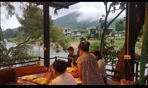 班康卡臣碧差汶府河小屋旅馆的一群人坐在河边的桌子旁