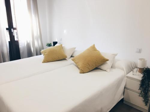 萨拉曼卡Apartamentos Pozo Amarillo的白色的床,配有白色床单和黄色枕头