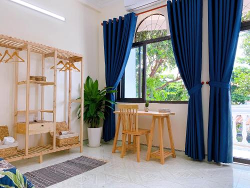 头顿Xoài Xanh Hostel & Villa的一间设有蓝色窗帘、桌子和窗户的客房