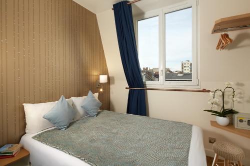 布洛涅-比扬古Hôtel Villa Sorel - Paris Boulogne的一间卧室配有一张带蓝色枕头的床和一扇窗户。