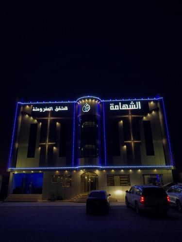 奈季兰Alshahamah Hotel Apartments的一座有照明的建筑,里面的汽车停在停车场