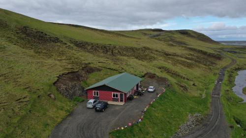 霍尔斯沃德吕尔Valkyrie Guesthouse - 1km from SELJALANDSFOSS的山丘上的一个红色房子,旁边停有汽车