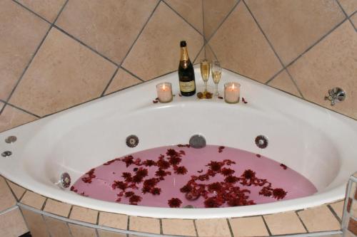 比勒陀利亚Batter Boys Guest House的装满红碎片的浴缸,装满葡萄酒瓶和蜡烛