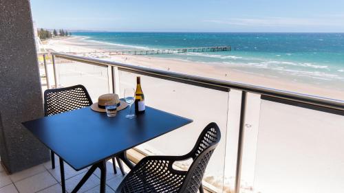 阿德莱德Oaks Glenelg Plaza Pier Suites的一张桌子和一瓶葡萄酒,坐在俯瞰着海滩的阳台