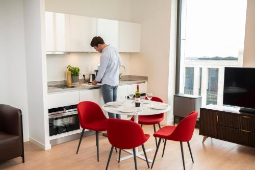 阿姆斯特丹PREMIER SUITES PLUS Amsterdam的男人在厨房里,有桌子和红色椅子