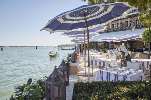 威尼斯Hotel Cipriani, A Belmond Hotel, Venice的一间位于水边的餐厅,配有桌子和遮阳伞