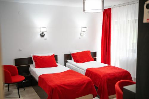 Cumpăna特拉斯吉拉斯皮斯科内格鲁旅馆的宿舍间内的两张床,配有红色床单和红色椅子