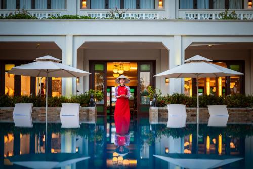会安RiverTown Hoi An Resort & Spa的站在建筑物前身穿红色衣服的女人