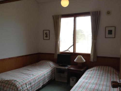 轻井泽草上飞酒店的配有书桌和窗户的客房内的两张床