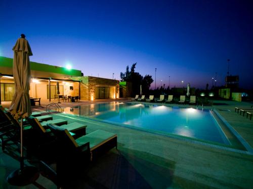 Al Qasţal安曼机场酒店的夜间游泳池,配有椅子和遮阳伞