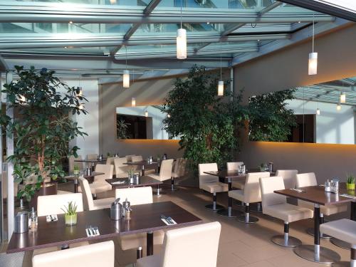 斯图加特斯图加特城市酒店的餐厅设有桌子和白色椅子,种有植物