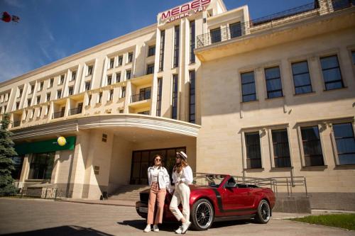 库斯塔奈麦迪奥酒店的两个女人站在一辆红车前面