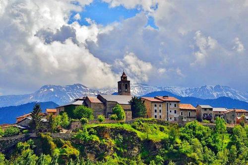 贝尔维尔德赛当亚Ático con encanto en Bellver de Cerdanya的山丘上的建筑,背景是山脉