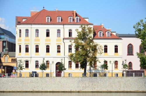 弗罗茨瓦夫翁德酒店及商务中心的河边一座黄色的建筑,有红色的屋顶