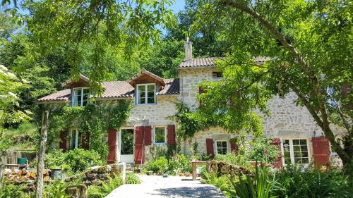 PensolLe Moulin de Pensol的一座石头房子,有红色百叶窗和树木