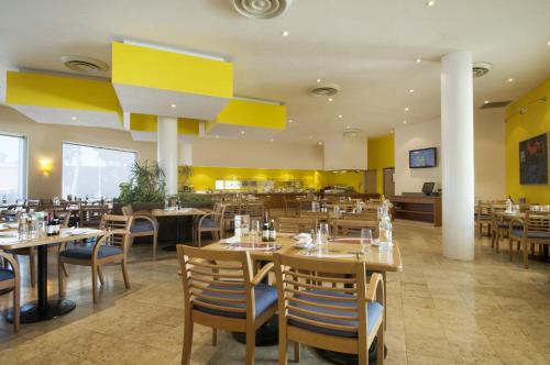 墨西卡利墨西卡利嘉年华酒店的餐厅设有木桌和椅子,墙壁为黄色