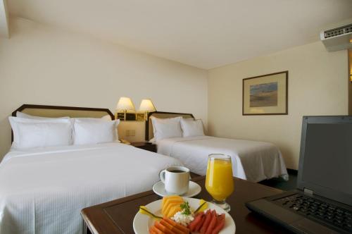 墨西卡利墨西卡利嘉年华酒店的酒店客房设有两张床和一张带一盘食物的桌子。