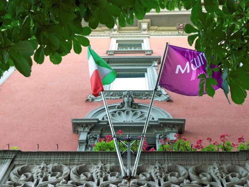 贝加莫贝加莫中心多尔斯宫美居酒店 的两面旗帜在一座粉红色的建筑前飞