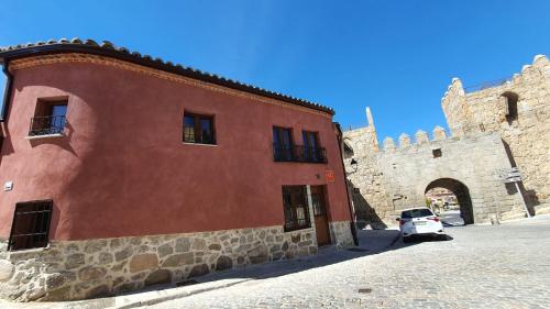 阿维拉Casas del Castillo, 3的一座红色的建筑,旁边停有一辆白色的汽车