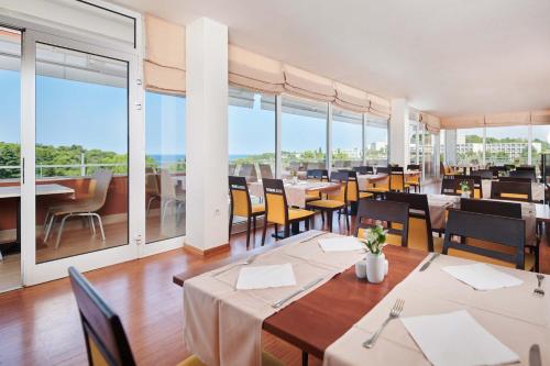 波雷奇Hotel Albatros Plava Laguna的餐厅设有桌椅和大窗户。