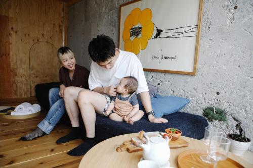 高松晴天旅舍的一名男子和两名妇女坐在一张长沙发上,带着婴儿