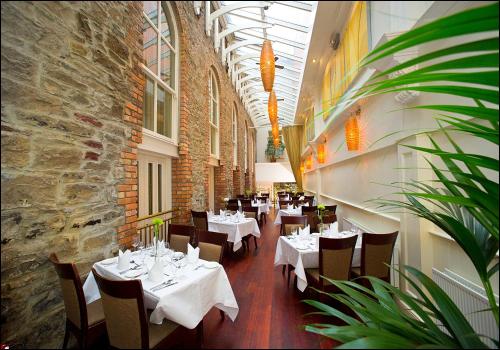 莫纳汉维斯特纳阿姆斯酒店的一间设有白色桌椅的餐厅,拥有砖墙