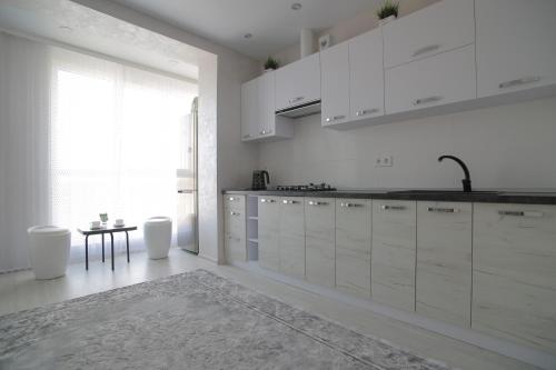 罗夫诺Ніжність的厨房配有白色橱柜、桌子和窗户。