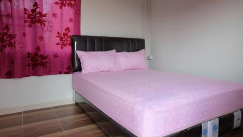 坤西育府那空那育度假村的一张粉红色的床,在房间里设有黑色床头板