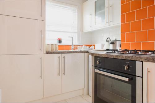 伦敦03 Bedroom Apartment-Self Check in的厨房配有白色橱柜和橙色瓷砖墙