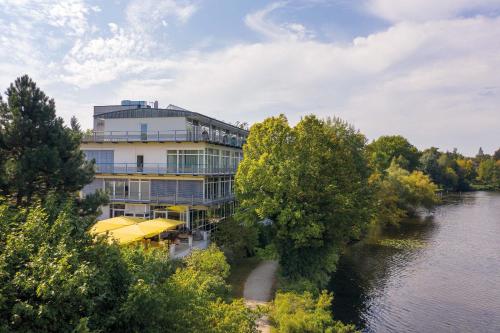 波茨坦Seminaris Hotel Potsdam Griebnitzsee的河边的一座建筑,上面有一把黄伞