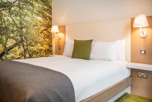 诺丁汉The Orchard Hotel & Restaurant的一间卧室配有一张带白色床单和绿色枕头的大床。