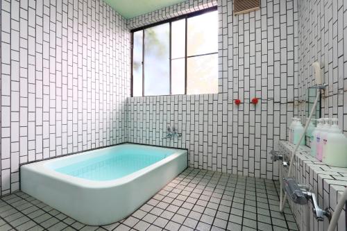 忍野村忍野湖酒店的白色瓷砖浴室设有浴缸和窗户。