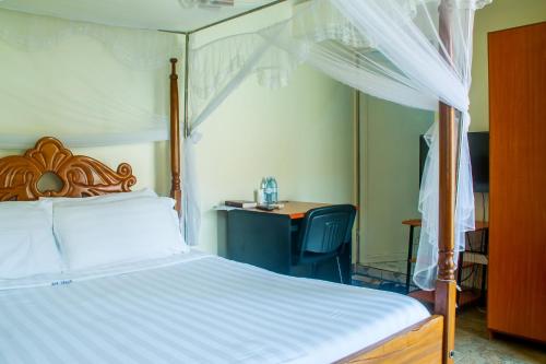 卡塞斯Sandton Hotel Kasese的一间卧室配有一张天蓬床和一张书桌