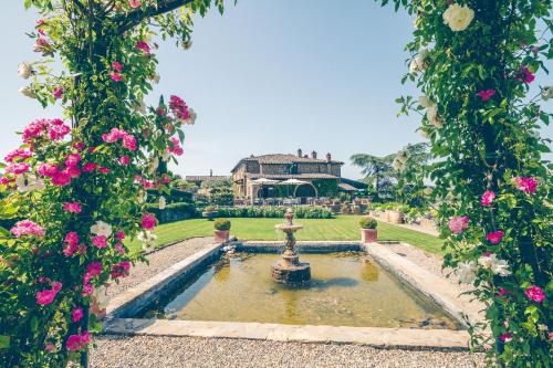 基安蒂盖奥勒卡潘尼尔葡萄酒度假酒店的一座花园,花园前方设有喷泉,房子前方有粉红色的花朵