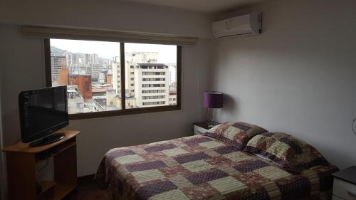 加拉加斯Apartosuites cerca del Boulevar de Sabana Grande y la Av. Solano的一间卧室设有一张床、一台电视和一个窗口。