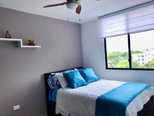 通苏帕DEPARTAMENTO TOTALMENTE NUEVO, AMOBLADO Y DE LUJO EN TONSUPA的一间卧室配有一张带蓝色枕头的床和一扇窗户。