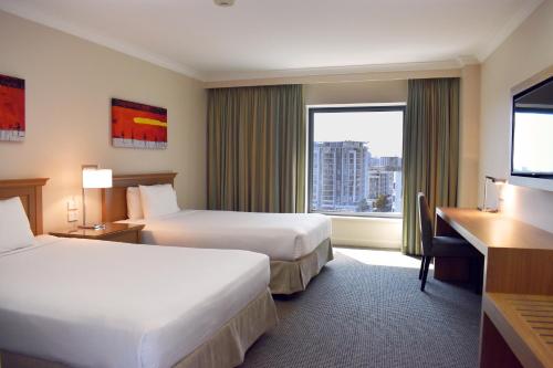 悉尼Stamford Plaza Sydney Airport Hotel & Conference Centre的酒店客房设有两张床、一张书桌和一个窗户。