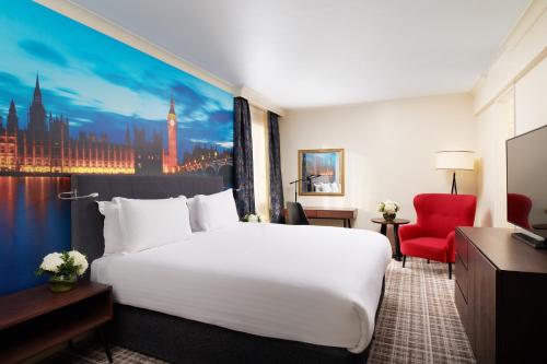 伦敦千禧国际伦敦格洛斯特酒店的酒店客房设有一张白色大床和红色椅子。