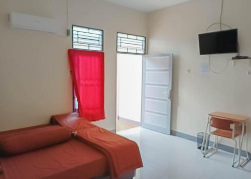 山口洋Homestay Verisha Mitra RedDoorz的一间卧室配有红色的床、一张书桌和一台电视。