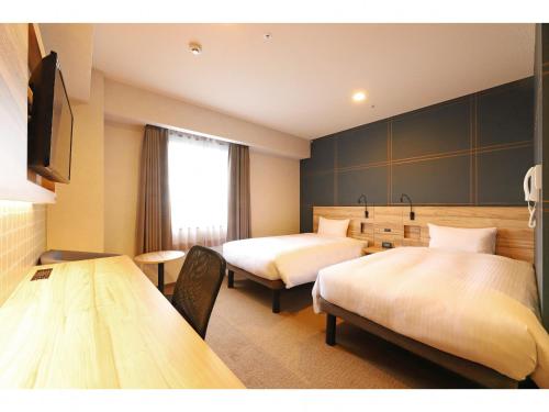 藤泽Smile Hotel Shonan Fujisawa的酒店客房设有两张床和一张桌子。
