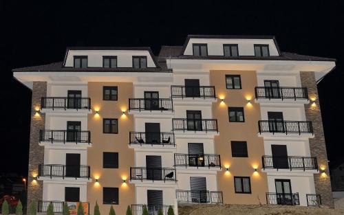兹拉蒂博尔NIDEHO Estate Apartmani的一座大型白色建筑,晚上设有阳台