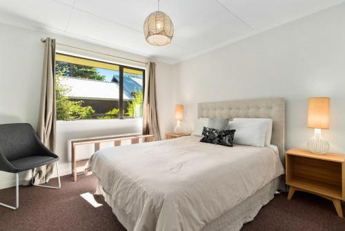 箭镇Rees on Reid - Arrowtown Holiday Home的一间卧室设有一张床、一个窗口和一把椅子