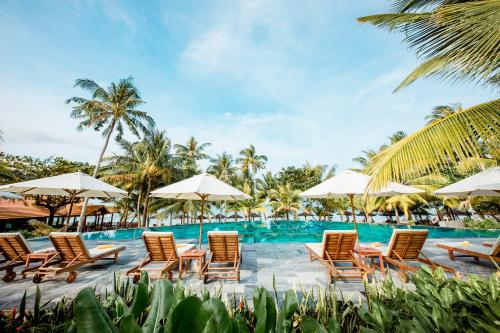 富国槟城侨海滩度假酒店的一组椅子和遮阳伞,位于游泳池旁