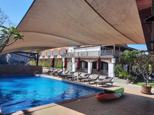 盼武里棕榈海滩度假村的一座带躺椅的游泳池位于大楼旁