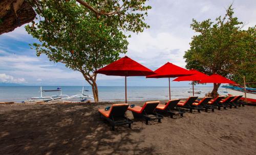 罗威那Bali Taman Lovina Resort & Spa Suites的海滩上一排椅子和红伞