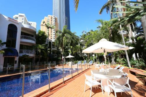 黄金海岸圣特罗佩度假酒店的一个带白色桌子和遮阳伞的游泳池以及建筑