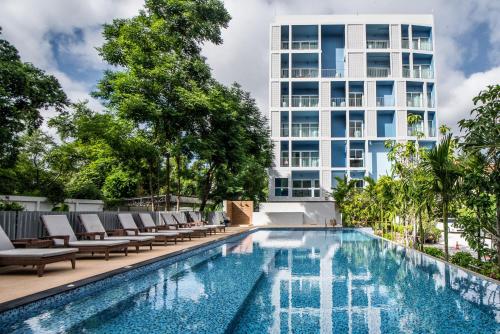 芭堤雅市中心DeeProm Pattaya Hotel的一座带躺椅的游泳池,一座高高的建筑