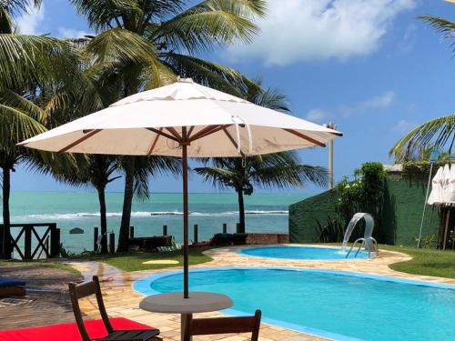 普拉亚多斯卡内罗斯Apart Hotel Praia dos Carneiros Apto 101的一把伞,坐在一个游泳池边,享有海景