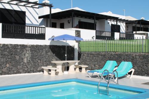 卡门港Villas Vistabella的一个带两把椅子和一张桌子的游泳池以及一把遮阳伞